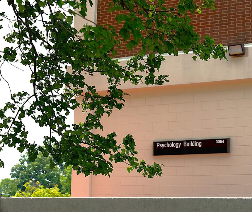 Photo of the Psychology Building sign with trees hanging over it.