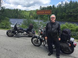 Dr. Brown standing beside his motorcycle in front of the Hudson River in the Adirondack Mountains