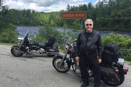 Dr. Brown standing beside his motorcycle in front of the Hudson River in the Adirondack Mountains