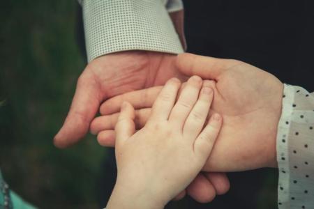 three outstretched hands resting on one another: a child's hand rests in the palm of an adult's hand, which is resting on the palm of an older adult's hand