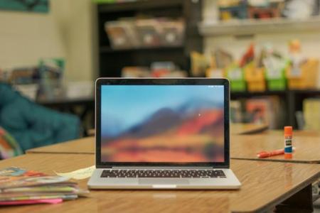 an open laptop rests on a desk at the center of a classroom